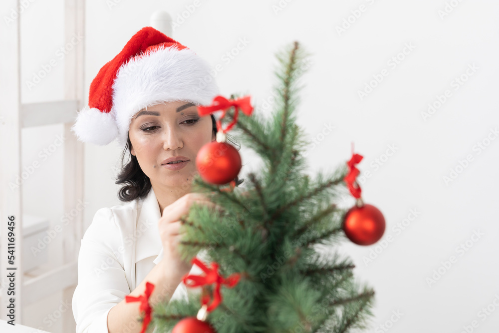 Portrait of smiling latin or indian business woman decorating christmas tree in office. Happy middle eastern woman decorating tree for christmas holiday. Multiethnic people celebrating holiday at work Portrait of smiling latin or indian business woman decorating christmas tree in office. Happy middle eastern woman decorating tree for christmas holiday. Multiethnic people celebrating holiday at work