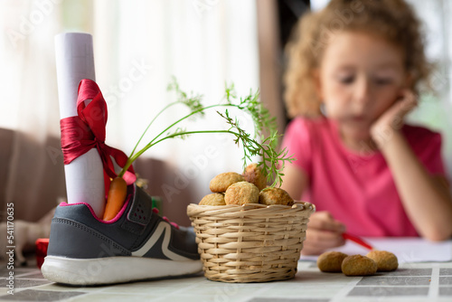 child writing letter on traditional Dutch holiday Sinterklaas in Europe, Netherlands, Belgium. girl put in in boot, shoe carrot for Santa horse, gift, pepernotin chocolate sweet cookies. soft focus
