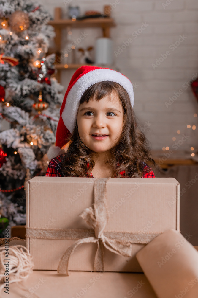 a happy little girl at home in the kitchen is packing Christmas presents in crab boxes. new year's sale a happy little girl at home in the kitchen is packing Christmas presents in crab boxes. new year's sale
