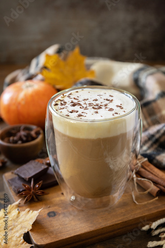 Pumpkin latte spice coffee, warm scarf and maple leaves on rustic background. Seasonal autumn concept with hot drink.