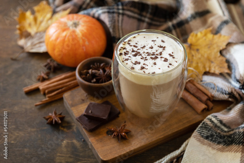 Seasonal autumn concept with hot drink. Pumpkin latte spice coffee, warm scarf and maple leaves on rustic background. Copy space.