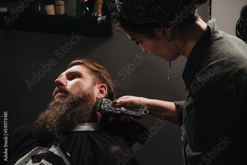 Side view of handsome bearded man having his beard cut by hairdresser at the barbershop