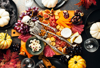 Halloween dark  table setting with cheese board decorated with spooky scary skeleton