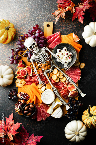 Fototapeta Naklejka Na Ścianę i Meble -  Halloween dark  table setting with cheese board decorated with spooky scary skeleton
