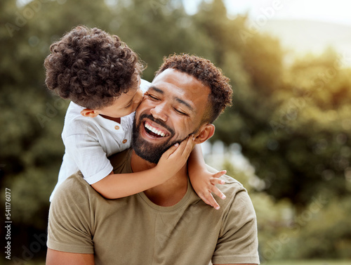 Father, bonding kiss and boy child hug happy in nature with quality time together outdoor. Happiness, laughing and family love of a dad and kid in a park enjoying nature hugging with care and a smile photo