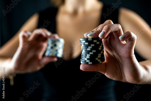 cropped portrait of woman in black dress holding chips in front of cleavage for gambling.