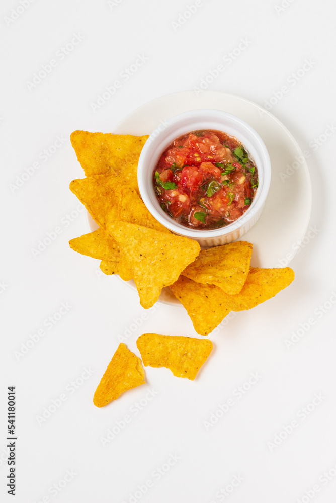 Nachos conventional Mexican triangular corn tortilla chips served with tomato salsa dip on white background; top view Nachos conventional Mexican triangular corn tortilla chips served with tomato salsa dip on white background; top view