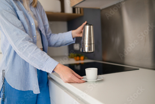 Attractive woman in the kitchen pouring a mug of hot coffee from a glass pot. Having breakfast in the morning. 