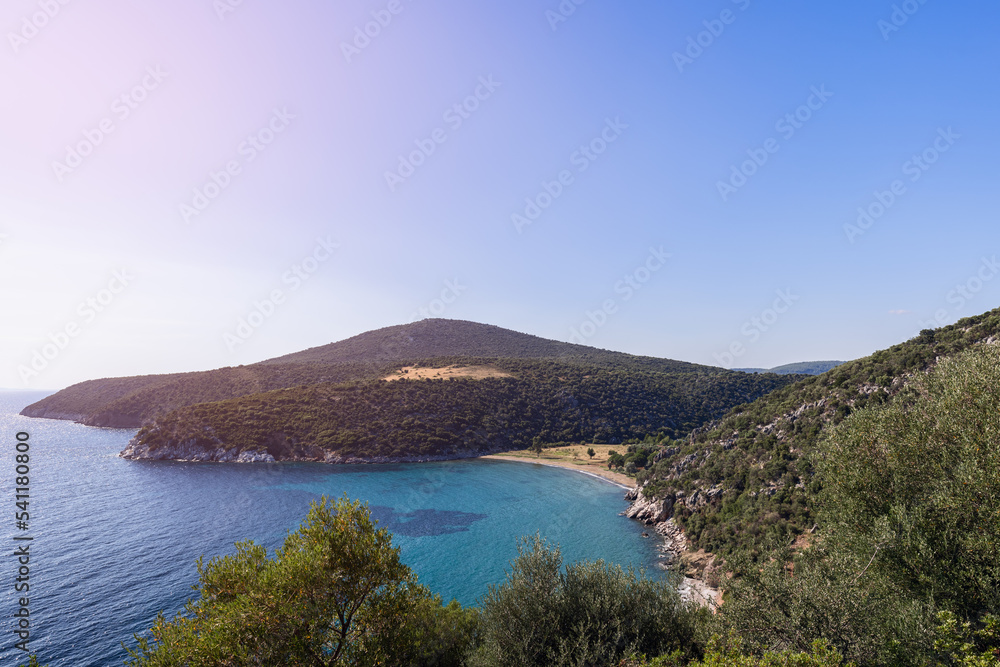 Low hills of rounded shape, covered with small trees and shrubs, descend to azure-colored sea, and hide sandy tiny beach among them, far from casual tourists view, Sithonia, Chalkidiki, Greece
