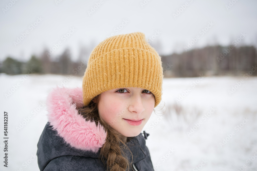 portrait of teenage child girl in winter clothes and hat against backdrop of nature and snow in winter