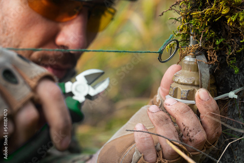 Close-up photo - a sapper clears a booby trap. The wire cutters cutting the wire of the frag grenade trap. photo