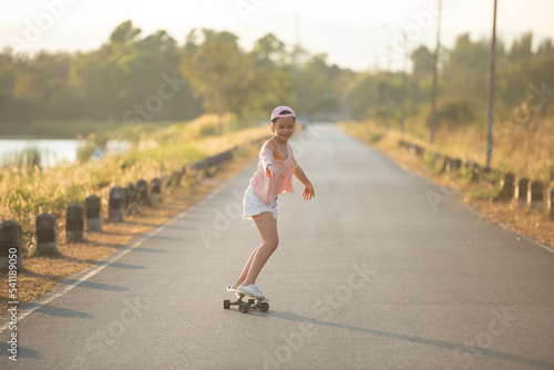 Teenager Beautiful happy Asian healthy woman smiling,riding and playing extreme sports skateboard as outdoor activity with happiness, relaxation during holidays in summer vacation at park morning time © nareekarn