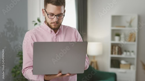 Young business man working at home with laptop and smiling, cuncluding sucessfull deal and gaining profit photo