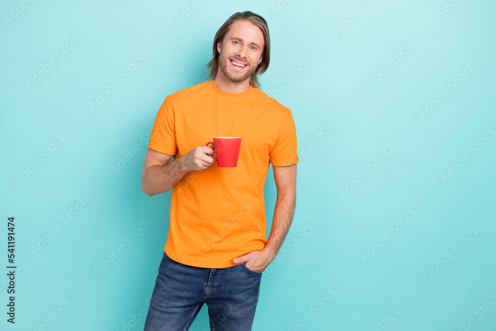 Photo of charming cheerful guy wear orange t-shirt drinking coffee empty space isolated teal color background Photo of charming cheerful guy wear orange t-shirt drinking coffee empty space isolated teal color background