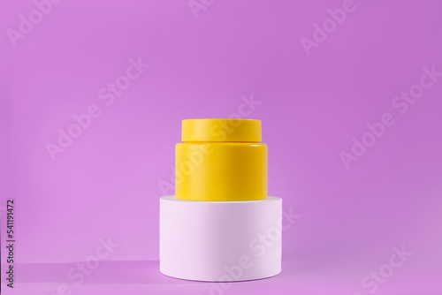 Yellow jar of cream on a stand, white podium on a pink background. Stylish look of the product, mock up, identity..