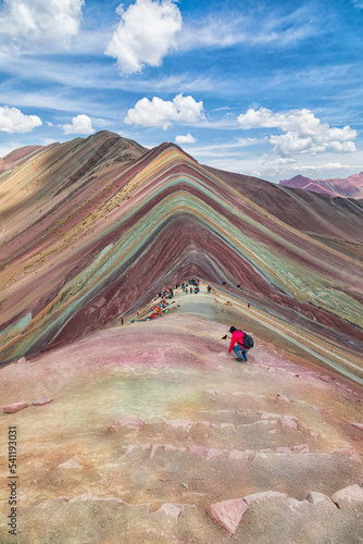 Tourist climbs in the foreground of the Rainbow Mountains at an altitude of 5000 meters.