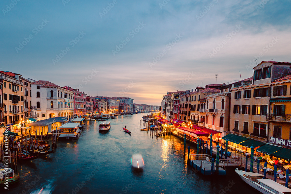 View of Venice's Grand Canal at sunset with illuminated venues on the shores and boats crossing it