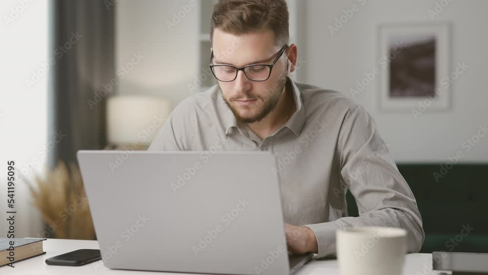 Smiling young man using laptop involved in internet lesson, motivated positive student studying online at home, looking at laptop screen and smiling Smiling young man using laptop involved in internet lesson, motivated positive student studying online at home, looking at laptop screen and smiling