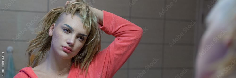 Fototapeta premium Young depressed female cancer patient standing in front of the bathroom mirror