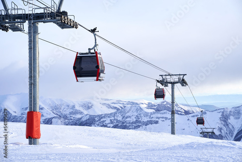 Cable car gondola at ski resort with snowy mountains on background. Modern ski lift with funitels and supporting towers high in the mountains on winter day. No people. photo