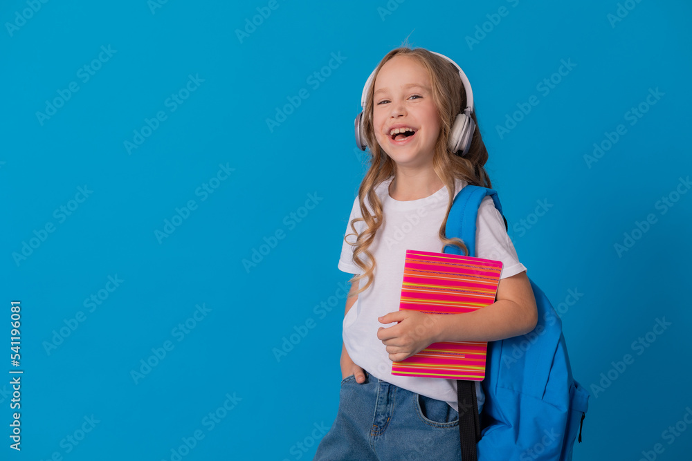 schoolgirl in a white T-shirt, headphones, with a backpack on her shoulder and a striped notebook schoolgirl in a white T-shirt, headphones, with a backpack on her shoulder and a striped notebook