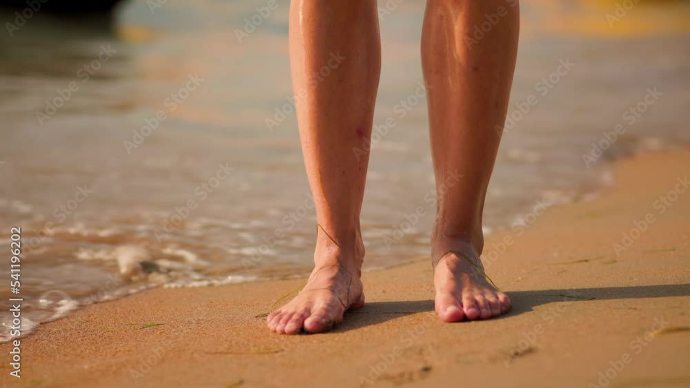 Beach and surf. Woman's tanned legs standing on the sand, washed by the waves of the sea. Close-up, slow motion. The concept of a summer vacation. Beach and surf. Woman's tanned legs standing on the sand, washed by the waves of the sea. Close-up, slow motion. The concept of a summer vacation.