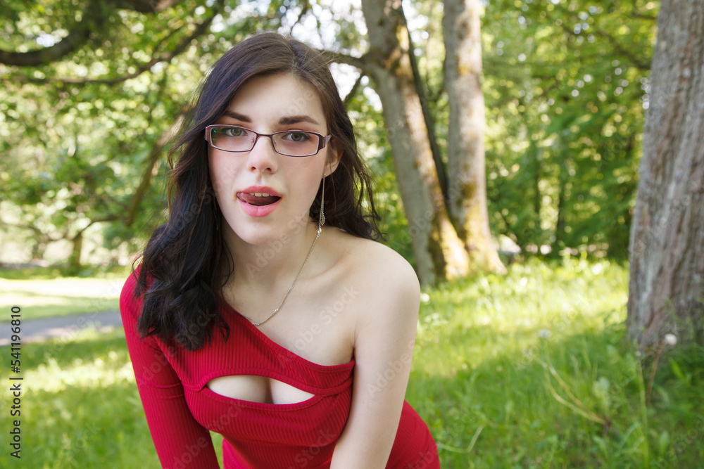 young brunette woman in a red dress walking in city park in summer young brunette woman in a red dress walking in city park in summer