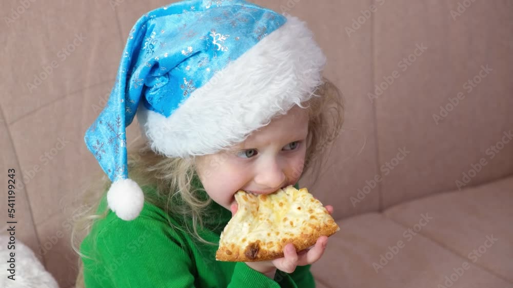 cute little girl eating pizza in blue santa hat waiting for christmas snack in anticipation of the holiday cute little girl eating pizza in blue santa hat waiting for christmas snack in anticipation of the holiday