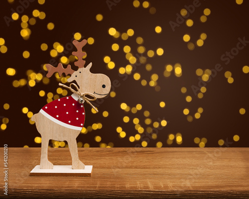 A wooden Christmas deer stands on a wooden table on a blurry bokeh background. Blurred light gold bokeh. © Olha Ye