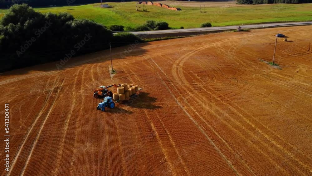 An aerial view of a large industrial golden field with a tractor collecting hay bales An aerial view of a large industrial golden field with a tractor collecting hay bales