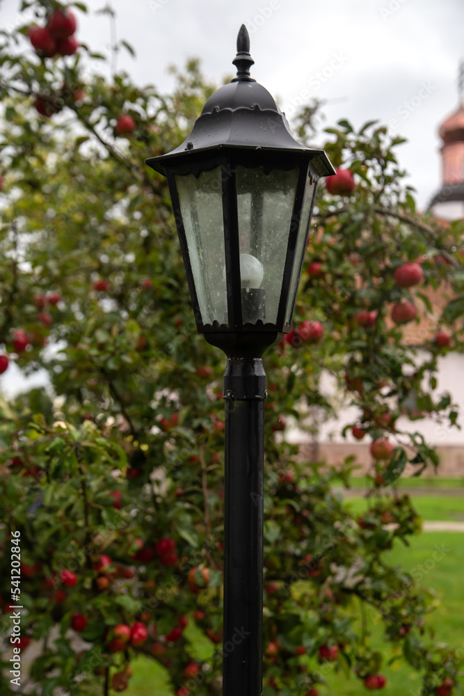 Street lamp in the garden. Against the background of an apple tree with red apples.