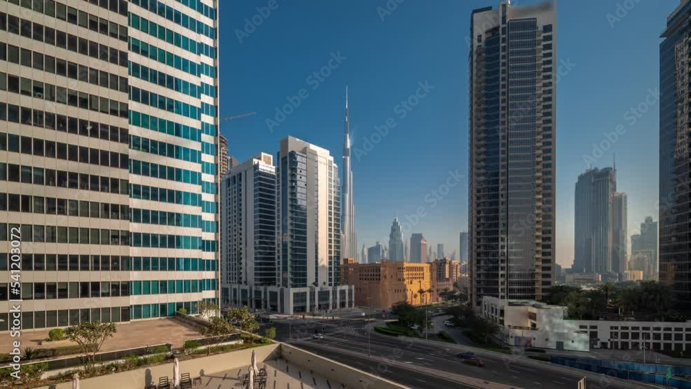 Aerial panoramic view to Dubai downtown and difc skyscrapers with busy traffic on intersection in Business bay district night to day transition timelapse during sunrise. Aerial panoramic view to Dubai downtown and difc skyscrapers with busy traffic on intersection in Business bay district night to day transition timelapse during sunrise.