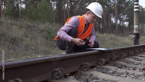 The railway transport inspector takes measurements with a tape measure of the railway track and makes entries in the log. photo