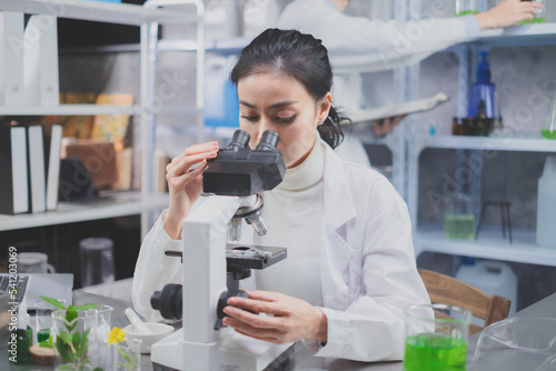 Female scientists is using microscope in laboratory. Concept of environmental biochemistry study plants and herb laboratory, Eco beauty serum, organic cosmatic and skin care product.