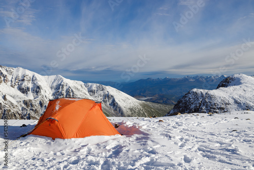 Orange tent on the background of a beautiful mountain snowy valley.