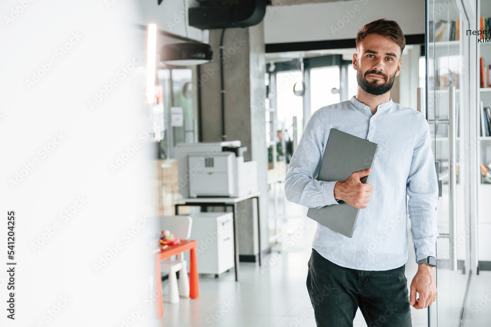 With laptop in hand. Young office worker in formal clothes is indoors