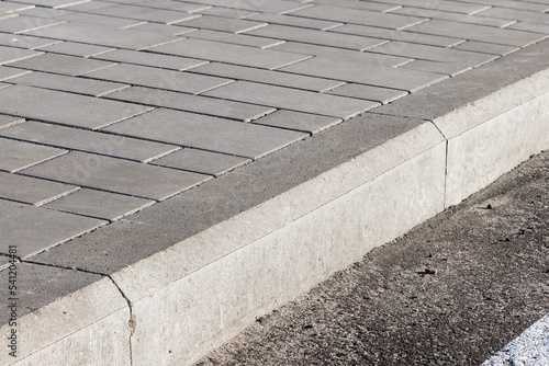 The sidewalk paved with concrete tiles is separated from the asphalt road by a concrete curb. photo