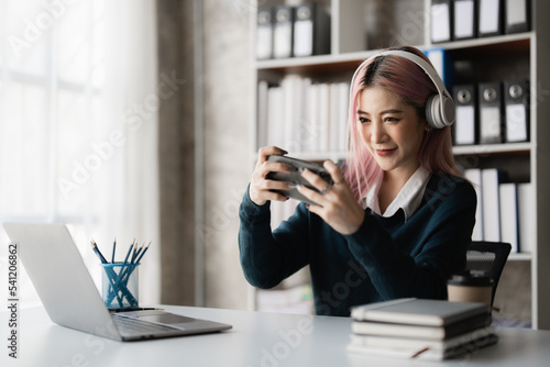 Photos Young excited asian woman wearing headphone is playing with his smart phone