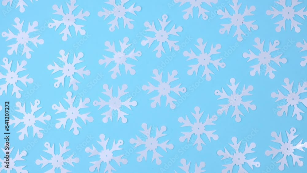 white decorative snowflakes randomly lie on a rotating blue background. top view. winter background with snowflake pattern. winter concept. flat lay. 4k.