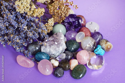 Semi-precious stones of different colors with dry lavender bouquet.  Amethyst and amethyst druse crystals, rose quartz, agate, apatite, aventurine,  turquoise,  rock crystal on a purple background. © Oksana