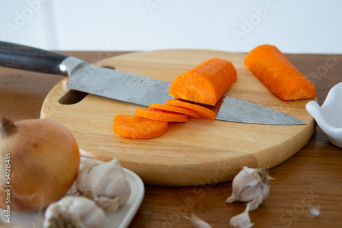 Sliced peeled carrot next to a knife on wood chopping board.