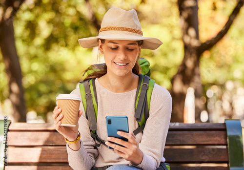 Fotografija Woman, phone and travel with coffee for backpacking in nature adventure relaxing on a park bench in the outdoors