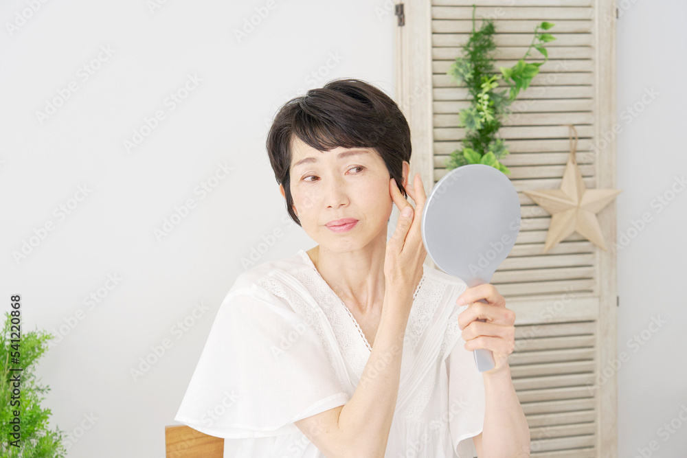 自宅で鏡を見て髪の毛をチェックする中年女性 自宅で鏡を見て髪の毛をチェックする中年女性
