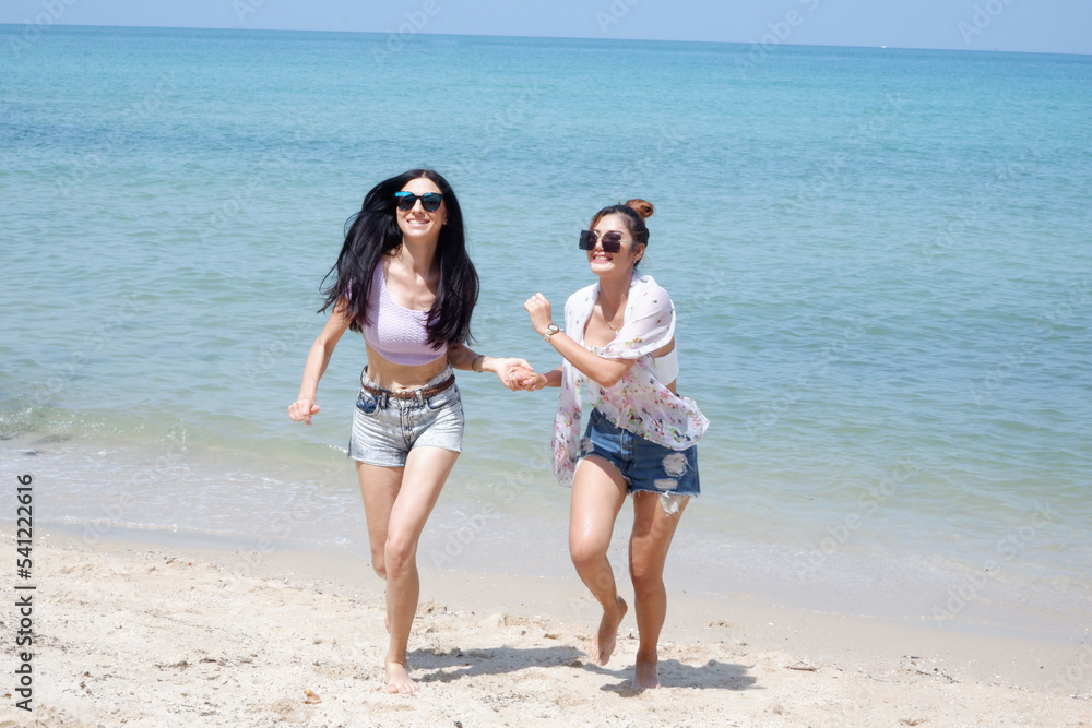 Young female tourists walking on the beach by the sea.