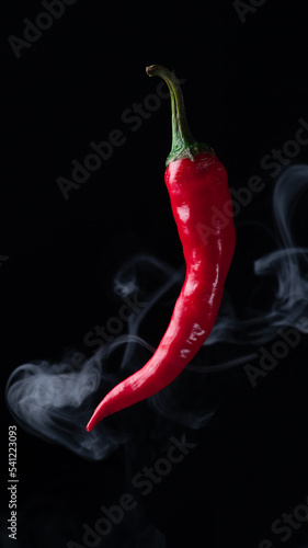 Red pepper flies on a dark background. There are rings of white smoke around the pepper