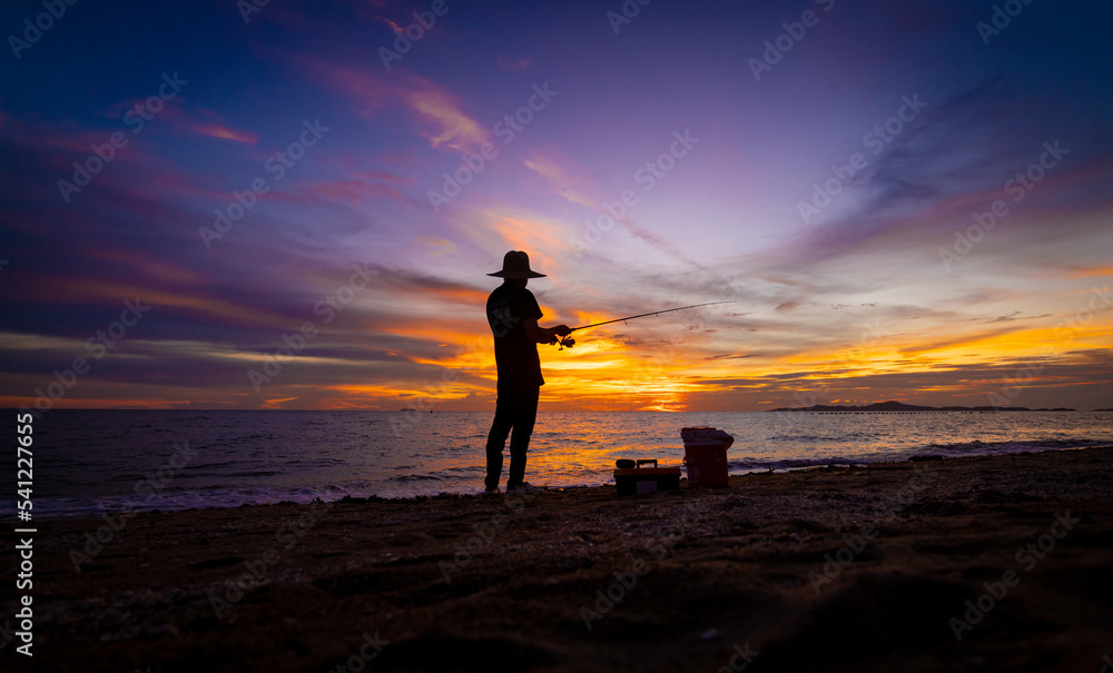 Silhouette fisherman stand fishing on beach with twilight sun sky in evening background.
