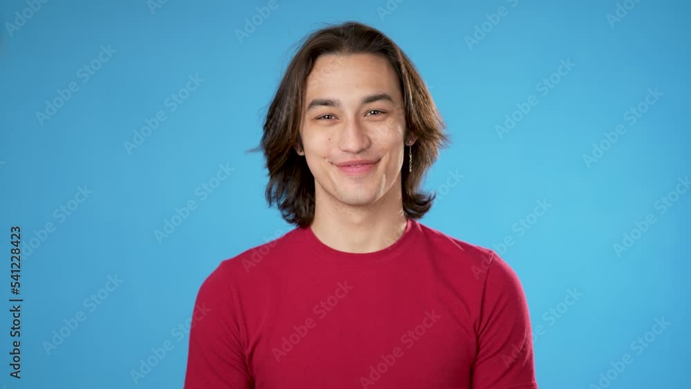 Portrait of smiling handsome Hispanic gender fluid young man 20s wearing red casual shirt isolated on blue color background in studio. Sincere emotions lifestyle concept. Looking camera Portrait of smiling handsome Hispanic gender fluid young man 20s wearing red casual shirt isolated on blue color background in studio. Sincere emotions lifestyle concept. Looking camera