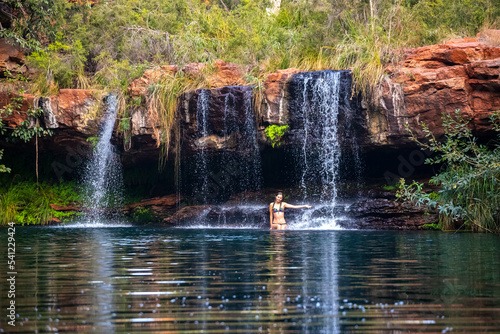 A beautiful girl in a bikini takes a refreshing dip in a rock pool under a waterfall in karijini national park  australia  playing in the water in a desert oasis in western australia