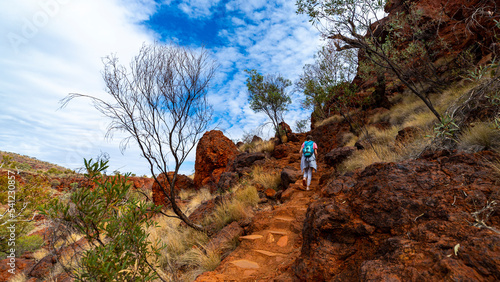 backpacker girl hiking on red rocks up a steep mountain in karijini national park in western australia, desert landscape of australian outback photo