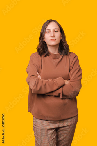 Vertical photo of young serious woman standing with crossed arms over yellow background